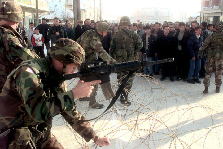 NATO soldiers uncoil two rows of concertina wire to maintain crowd control as residents of Vitina, Kosovo, protest in the streets on Jan. 9, 2000.